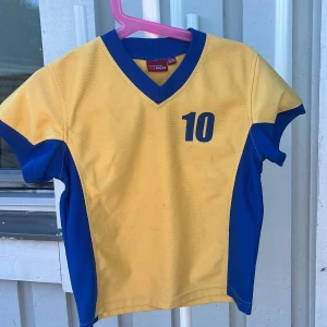 Svensk fotbollströja gul/blå My Wear - Gul och blå fotbollströja från My Wear med nummer 10 på bröstet och SWEDEN tryckt på ryggen. Tröjan har V-ringning med blå ribbad kant och korta ärmar. Perfekt för att visa support för Sverige på matchen eller träningen.