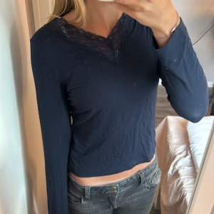 Mörkblå långärmad topp med spets från Gina tricot - Mörkblå långärmad topp från Gina Tricot med snygg v-ringning och spetsdetaljer runt halsen. Mjuk och skön bomullskänsla, perfekt till jeans eller kjol. Enkel men ändå lite extra tack vare spetsen.