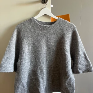 Grå stickad tröja & Other Stories - Mysig grå stickad tröja från & Other Stories med rund halsringning och halvkort ärm. Tröjan har en lite loose passform och är perfekt för lager-på-lager under hösten och vintern. Enkel att matcha med både jeans och kjol. Har ingen defekter och har använts ett fåtal gånger! 