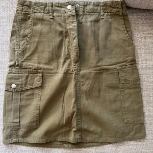 Army green/Olivgrön cargokjol från Lipp - Olivgrön cargokjol från Lipp med stora fickor på sidorna, bälteshällor och dragkedja fram. Stl 36