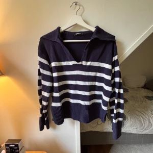 Randig stickad tröja från Gina Tricot - Mörkblå och vit randig stickad tröja från Gina Tricot med v-ringning och krage. Tröjan har långa ärmar och bred ribbad nederkant, perfekt för en chill och stilren look. Jättebra skick! 