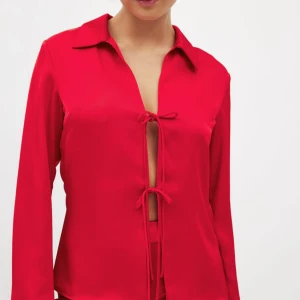 Röd satinblus med knytning från NA-KD - Snygg röd långärmad blus i satin från NA-KD med två knyt framtill och djup v-ringning. Nypris 499!