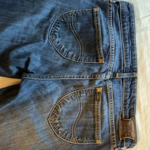 Blå jeans från Lee - Säljer ett par klassiska blå jeans från Lee med bootcut stil och snygga bakfickor med Lee-logga. Jeansen har en låg midja, normal passform och är tillverkade i slitstarkt denimtyg. Mått: midja - 39,5 cm innerbenet - 75.