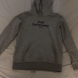 Grå hoodie från Peak Performance - Säljer en grå hoodie från Peak Performance med svart logga på bröstet då den inte passar mig längre. Perfekt för chill dagar eller när du vill ha en enkel och snygg look. Skön och i bra skick. Sitter som storlek S