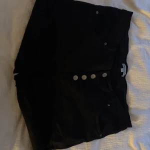 Svarta högmidjade shorts med knappar - Svarta shorts med hög midja och fyra snygga silverfärgade knappar framtill. Klassisk jeansmodell med fickor både fram och bak. Perfekta för sommaren och lätta att matcha med allt.