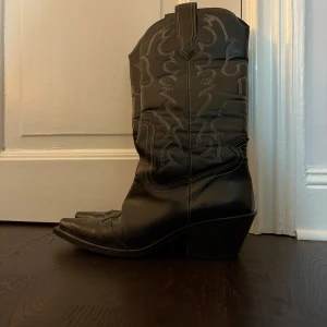 Boots svarta - Snygga svarta cowboy boots med dekorativa sömmar och spetsig tå. Klassisk westernstil med markerad klack och högt skaft.