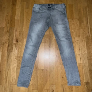 Gråa jack n jones jeans - Snygga grå jeans med tvättad effekt och klassisk femficksdesign. Jeansen har smal passform och raka ben, perfekt för en clean och modern stil. Tillverkade i mjukt denimtyg med stretch för extra komfort. Storleken är W30 L31