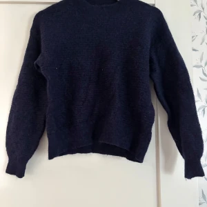 Mörkblå stickad tröja från Lindex - Mysig mörkblå stickad tröja från Lindex i storlek M. Tröjan har en klassisk rund halsringning och långa ärmar. Perfekt för lager-på-lager och passar till både jeans och kjol. Materialet känns mjukt och värmande. Liten i storleken.