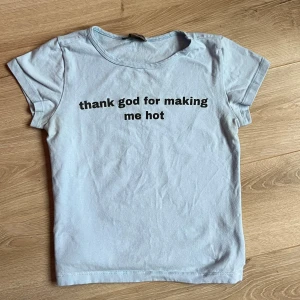 Ljusblå t-shirt från Romantic Blue - Säljer en ljusblå t-shirt från Romantic Blue med texten 'thank god for making me hot' tryckt på framsidan. T-shirten har en klassisk rund hals och korta ärmar. Supersnygg till jeans 