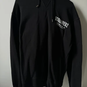 Dsquared2 - Snygg svart hoodie från Dsquared2 med tryck på bröstet. Den har en klassisk design med dragsko i huvan och ribbade muddar vid ärmslut och nederkant. Perfekt för en stilren look.