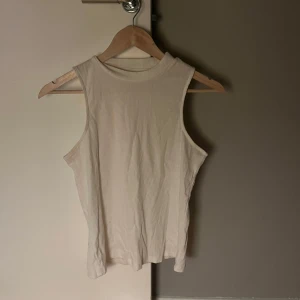 Vit ärmlös topp - Säljer en stilren vit ärmlös topp i ribbat material. Perfekt för varma dagar eller som lager under en jacka. Enkel och mångsidig design som passar till det mesta.