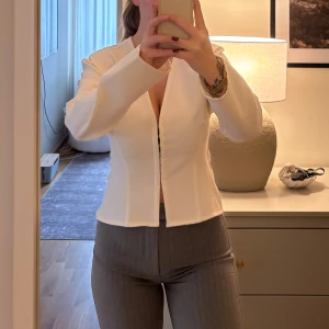 Elegant topp från Zara - Säljer en stilren vit topp från Zara med ”knappar” framtill. Toppen har en figurnära passform och långa ärmar. Perfekt för en chic look. Aldrig använd