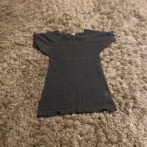 Mörkgrå stickad topp från Lindex - Säljer denna super söta mörkgrå stickad topp från Lindex. Toppen har korta ärmar och ett diskret mönster som ger en fin textur. Perfekt för en stilren look.