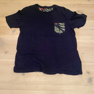 Jack and Jones tshirt - Snygg svart/mörkblå t-shirt från Jack & Jones med en cool mönstrad bröstficka i grönt och beige. Skönt material perfekt för sommaren. Skriv för frågor och mått osv
