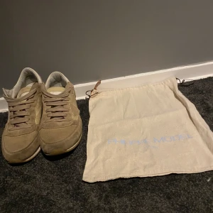 Beige sneakers från Philippe Model - Snygga beige sneakers från Philippe Model i mocka med snörning. Skorna har en klassisk design med vit sula och är perfekta för en stilren look. De kommer med en praktisk tygpåse för förvaring. (endast dustbag medföljer)