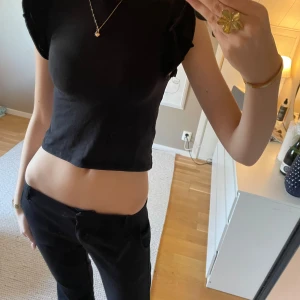 Svart croppad topp med volangärmar - Snygg svart croppad topp med volangdetaljer på ärmarna. Perfekt för en stilren look. Toppen är ärmlös och har en tight passform.