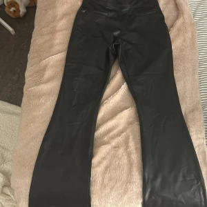 Svarta bootcut byxor i skin material storlek 165 - Snygga svarta bootcut byxor i syntetmaterial. Perfekta för en trendig look med mid waist passform. Går att vika ner till low waist  SKRIV TILL MIG INNAN NI KÖPER