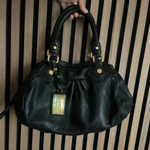 Marc Jacobs väska  - Marc Jacobs classic q baby groove med guldiga detaljer. Väskan är svart. Axelremband ingår. Den är ca 30 cm bred och är i den lilla modellen. Mycket bra skick. Fler bilder finns och svarar gärna på frågor 🖤