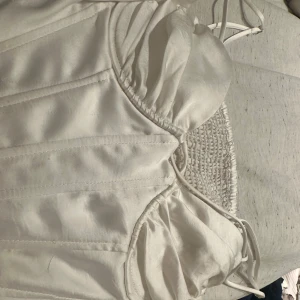 Vit korsettopp från Zara - Säljer en stilren vit korsettopp från Zara med smala axelband och rynkade detaljer vid bysten. Toppen har en elegant design och är perfekt för att lyfta vilken outfit som helst. Passar bra till både jeans och kjol. 🐻