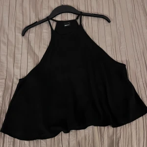 Topp - Snygg svart ärmlös topp från Gina Tricot i storlek L. Perfekt för en stilren look med tunna axelband och en luftig passform. Passar utmärkt till både jeans och kjol. Ett måste i garderoben för alla modeälskare! Kortare modell. Endast använd 1 gång. Lite större öppning under armhålorna (se bilder). Lite högre krage vid halsen 