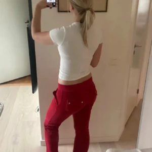 Röda mjukisbyxor från Juicy Couture - Snygga röda mjukisbyxor från Juicy Couture med snörning i midjan. Perfekta för en avslappnad stil. Byxorna har en bekväm passform och är tillverkade i ett mjukt material.