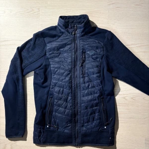 Tenson hybridjacka - Mörkblå Tenson hybridjacka i storlek S säljes. Jackan har två små hål som knappt syns samt ett litet i ena ärmen. I övrigt lite använd.