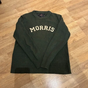 Morris tröja - Säljer en snygg grön stickad tröja från Morris med texten 'MORRIS' i vitt på bröstet. Tröjan har långa ärmar och ribbade muddar vid ärmslut och nederkant. Perfekt för kyligare dagar!
