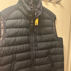 Svart parajumper väst - Snygg svart parajumper väst i princip oanvänd med dragkedja och hög krage. Perfekt för kyligare dagar och har en stilren design med diskreta detaljer. Västen har praktiska fickor med dragkedjor.