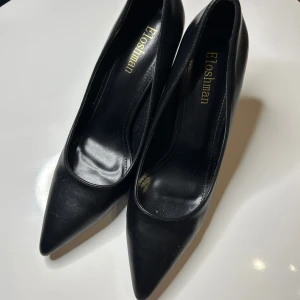Svarta pumps från Eloshiman - Eleganta svarta pumps från Eloshiman med spetsig tå och hög klack (8-9cm). Perfekta för en stilren look. Tillverkade i ett slätt material som ger en sofistikerad känsla.