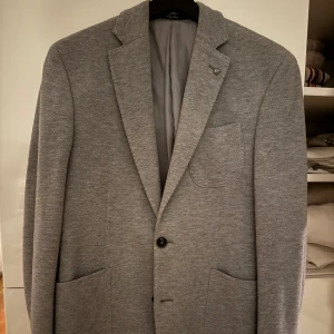 Grå kavaj från MNG Man - Snygg grå kavaj från MNG Man i en klassisk design. Kavajen har två knappar framtill och en bröstficka. Perfekt för både formella och semi-formella tillfällen.