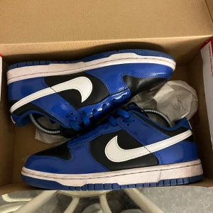 Nike Dunk i blått och svart - Snygga Nike Dunk sneakers i en fräsch kombination av blått och svart med vit swoosh. Perfekta för en stilren look. Skorna har en klassisk design med snörning och en bekväm passform. 