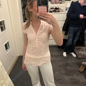 Beige blus från H&M - Säljer en stilren beige blus från H&M i storlek S. Blusen har korta ärmar och en v-ringad design med knappar framtill. Perfekt för en elegant och avslappnad look. Blusen är lite 2000tals style🤩