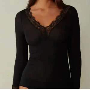 Svart långärmad topp med spetsdetaljer - Elegant svart långärmad topp med v-ringad spetsdetalj. Perfekt för en stilren look.