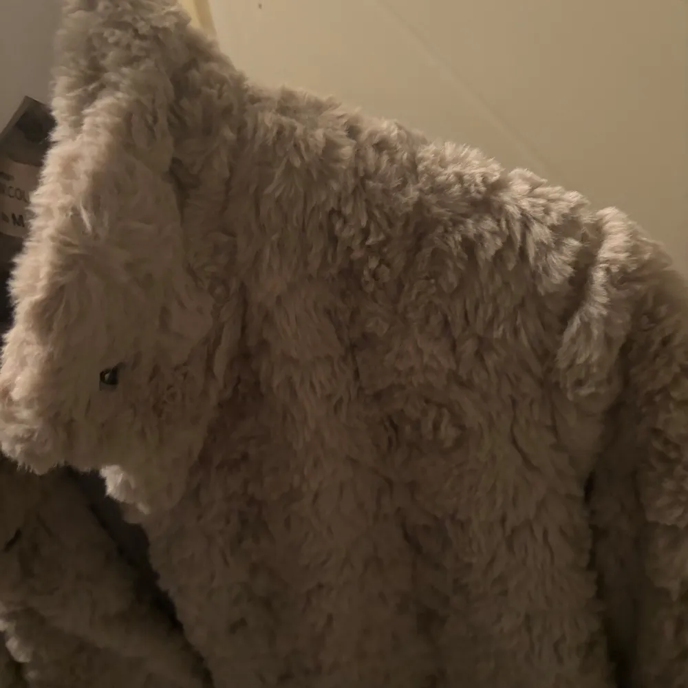 Mysig beige teddyjacka. Perfekt för kyliga dagar med sin fluffiga och varma design. Jackan har en klassisk krage och långa ärmar.. Takit.