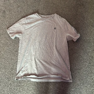 Grå t-shirt från Ralph Lauren - Säljer en klassisk grå t-shirt från Ralph Lauren med en broderad logotyp på bröstet. T-shirten är kortärmad och tillverkad i mjukt material för en bekväm passform. Den är i storlek xl i barn storlek vilket motsvarar S/M