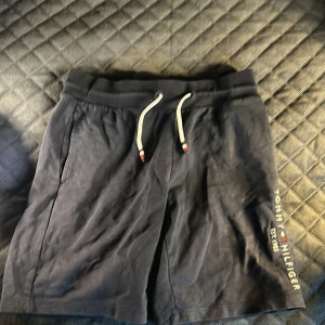 Svarta shorts från Tommy Hilfiger - Snygga svarta shorts från Tommy Hilfiger med snörning i midjan och broderad logga på sidan. Samt så har den 3 fickor en där bak två där fram. Perfekta för en avslappnad stil.