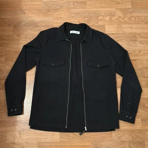 Svart overshirt från Samsøe Samsøe - Snygg svart overshirt från Samsøe Samsøe med dragkedja och två bröstfickor med knappar. Perfekt för lager-på-lager-stil. Långärmad design som funkar året runt. Inga fläckar eller slitage. Skriv gärna om ni har frågor allt ifrån pris till fler bilder. 