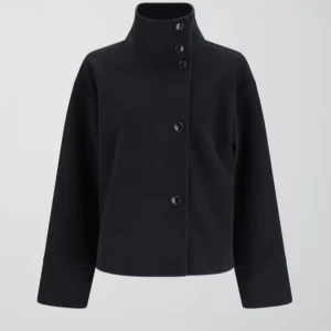 Mörkblå kappa från Gina Tricot - Snygg svart kappa från Gina Tricot med hög krage och knappar framtill. Perfekt för en stilren look. Jackan har långa ärmar och en rak passform. Nypris 599kr men säljer för 450