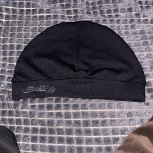 Svart mössa med tryck från sixtis - Snygg svart mössa med ett diskret tryck på framsidan. Perfekt för kyliga dagar och enkel att matcha med olika outfits.