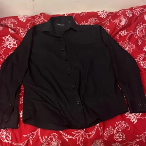 Svart skjorta från Dressmann - Snygg svart skjorta från Dressmann i storlek M. Skjortan har långa ärmar och knappar framtill. Perfekt för en stilren look.