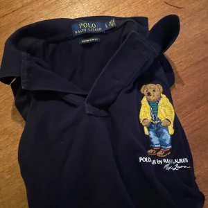 Mörkblå pikétröja från Ralph Lauren - Säljer en mörkblå pikétröja från Ralph Lauren med den klassiska björnen broderat på tröjan. Hör av dig om du har någon fråga. 
