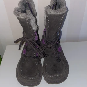 Grå vinterstövlar med lila detaljer - Säljer ett par grå vinterstövlar med lila detaljer och snörning st.29,5 De har en mysig pälsfodring och dekorativa mönster i rosa och lila på baksidan. Perfekta för kalla dagar.