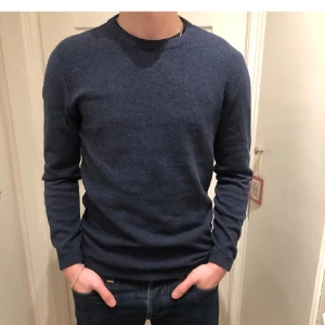 Mörkblå stickad tröja - Säljer en stilren mörkblå stickad tröja från dressman med rund hals och långa ärmar. Perfekt för kyligare dagar och passar bra till jeans.