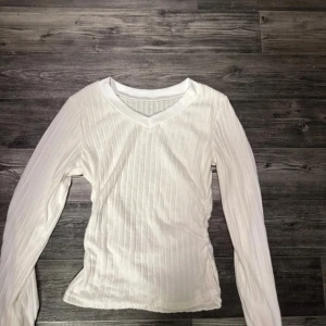 Vit ribbad långärmad tröja - Säljer en stilren vit ribbad tröja med v-ringning och långa ärmar. Perfekt för lager-på-lager eller som den är. Passar till många olika outfits! 