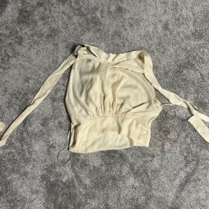 Beige blus med knytband - Elegant beige blus med knytband i midjan och långa ärmar. Blusen har en lätt och luftig design, perfekt för vår och sommar. Den har en vacker drapering och en mjuk, feminin stil.