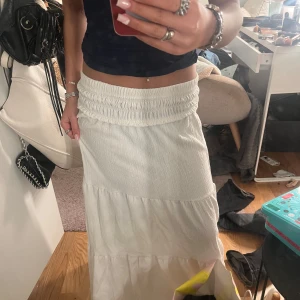 Vit långkjol - Säljer en vit långkjol med resårmidja som ger en bekväm passform. Kjolen har en luftig design med flera lager som ger ett fint fall. Perfekt för en avslappnad stil.