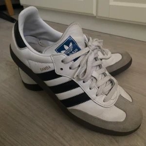 Adidas Samba sneakers - Klassiska Adidas Samba sneakers i vitt och svart med grå detaljer. Köpta från Zalando något år tillbaka för 1 325 kr. Använda men inte söndags på något sätt. De mest bekväma skorna nånsin! Har inte testat att putsa upp dom än.