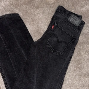 Svarta jeans från Levi's - Snygga svarta jeans från Levi's med klassisk femficksdesign och knappgylf. Perfekta för en stilren look. De har en rak passform och är tillverkade i slitstarkt denim.