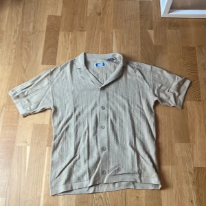 Beige kortärmad skjorta från Jack & Jones - Säljer en stilren beige skjorta från Jack & Jones. Skjortan har korta ärmar och knappar framtill. Perfekt för en avslappnad stil med en klassisk touch. Tillverkad i ett bekvämt material.