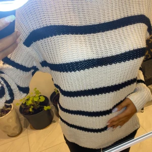 Randig stickad tröja - Säljer en mysig stickad tröja i vitt med svarta ränder. Tröjan har en avslappnad passform och långa ärmar, perfekt för kyligare dagar. Den är både stilren och bekväm, ett måste i garderoben!